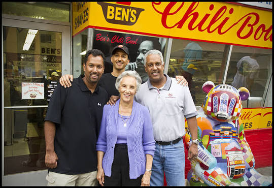 Four people standing together outside Ben’s Chili Bowl next to a colorfully painted bear statue