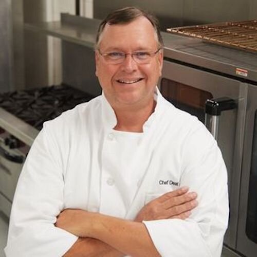 Chef Steve Deal, smiling with arms crossed in a white chef coat inside a commercial kitchen