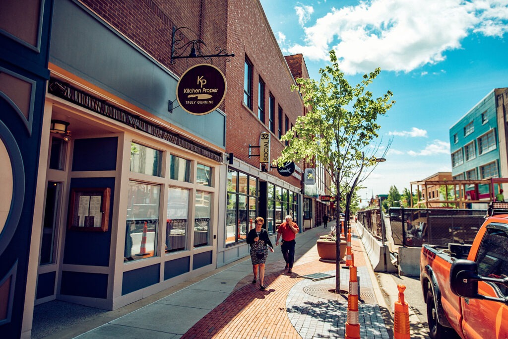 The Kitchen Proper sign hanging from a brick building on a sunny downtown Battle Creek sidewalk