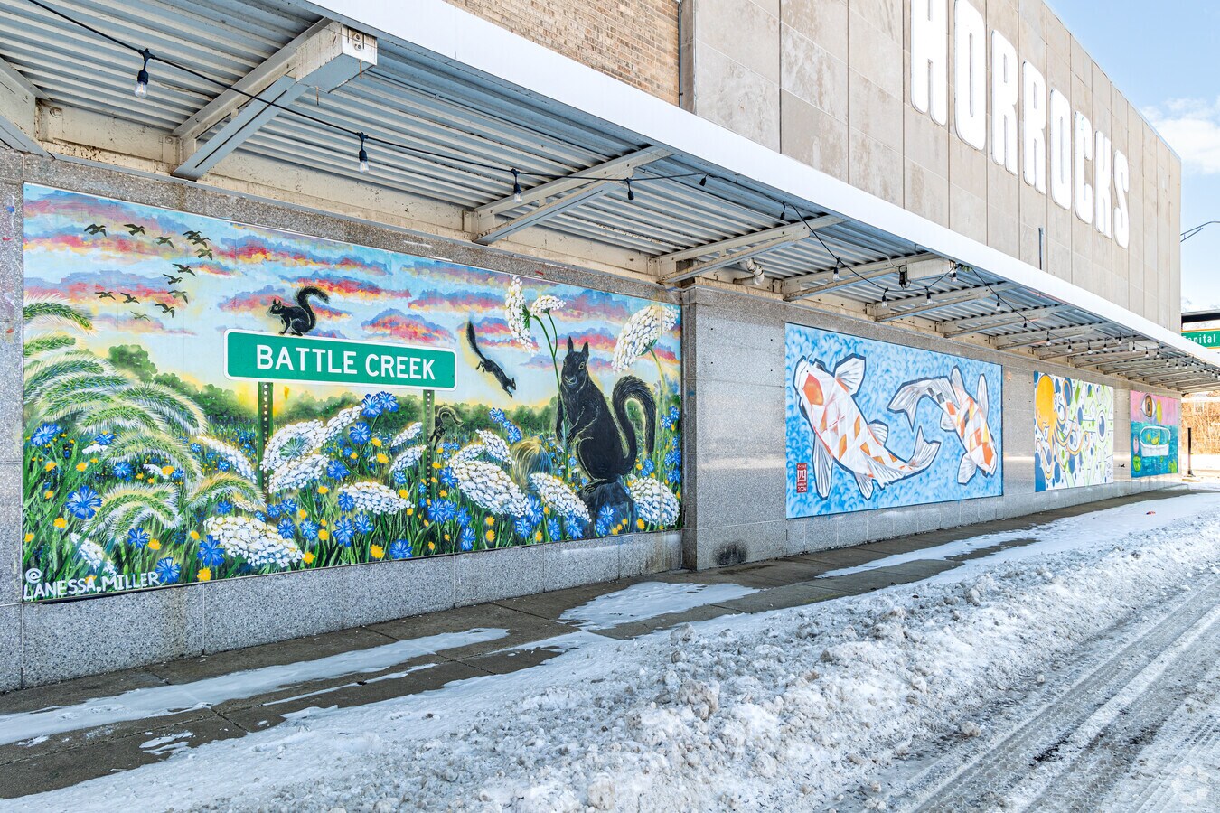 A colorful downtown Battle Creek mural showing a Battle Creek road sign, a black squirrel, and wildflowers at sunset