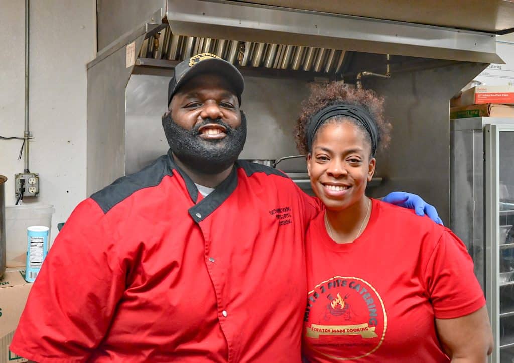 Two local restaurant owners in red chef shirts smiling together in their commercial kitchen